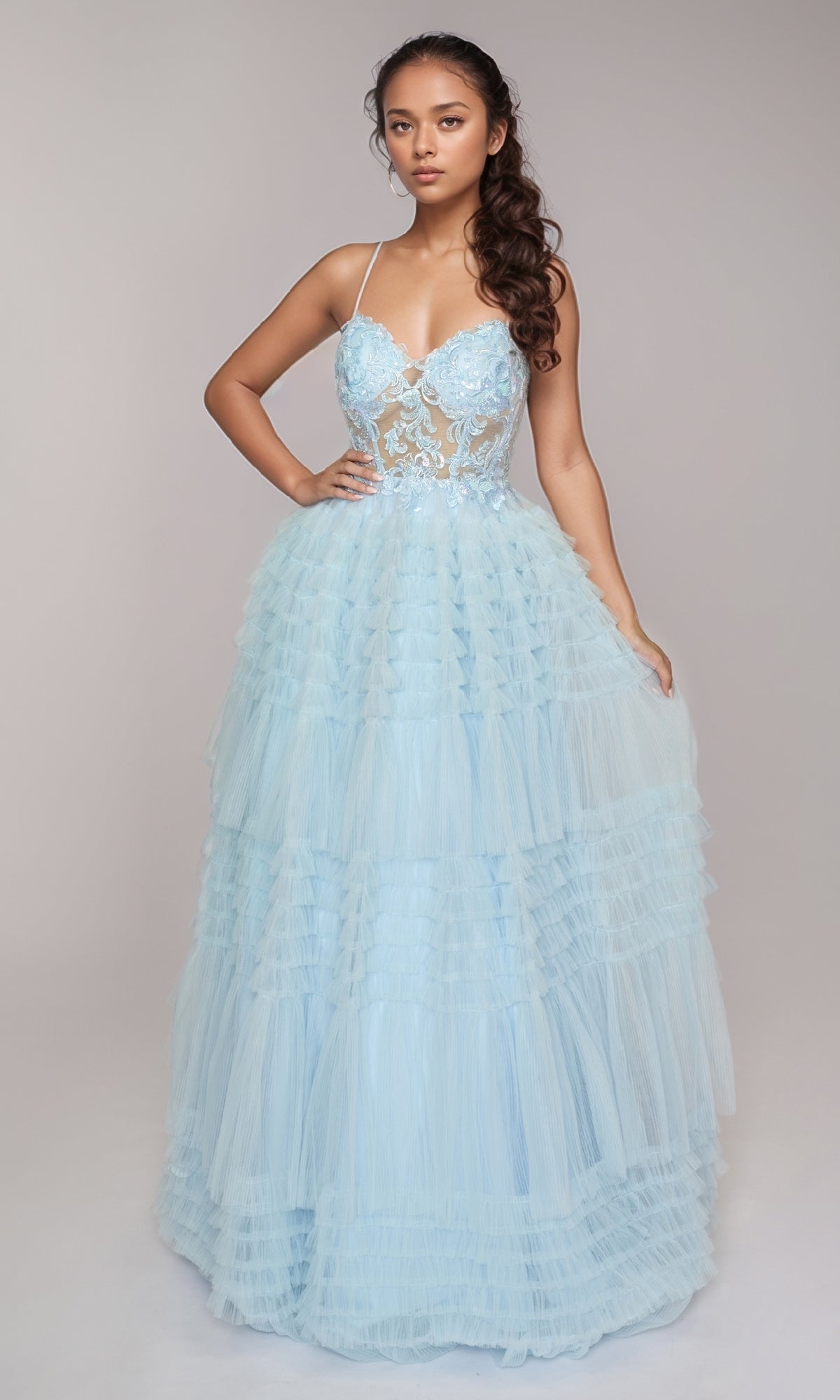 A woman wears the Nina Canacci 1582, a light blue long formal dress with an embellished fitted bodice and an A-line ruffle tiered skirt, set against a neutral background.